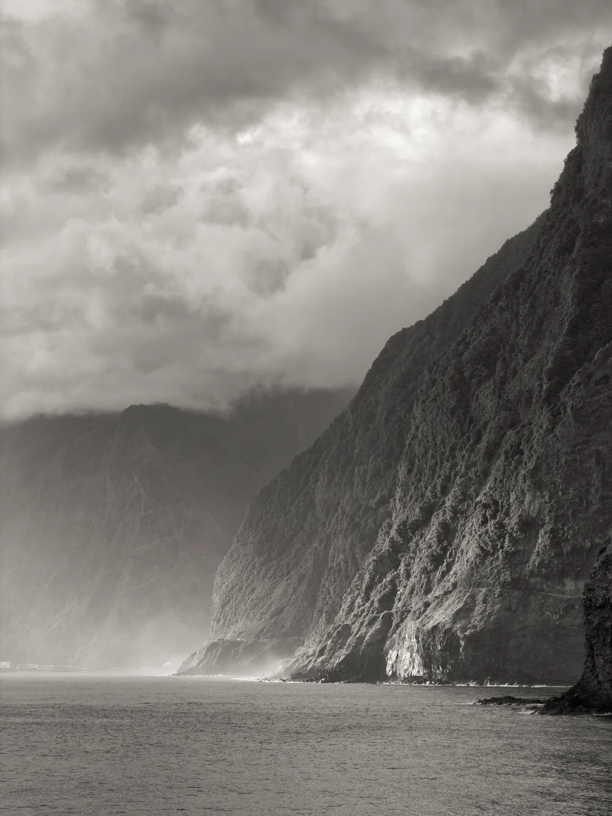 A soft luminous sepia coastal print with open haze, controlled cloud light, and a gently defined cliff.