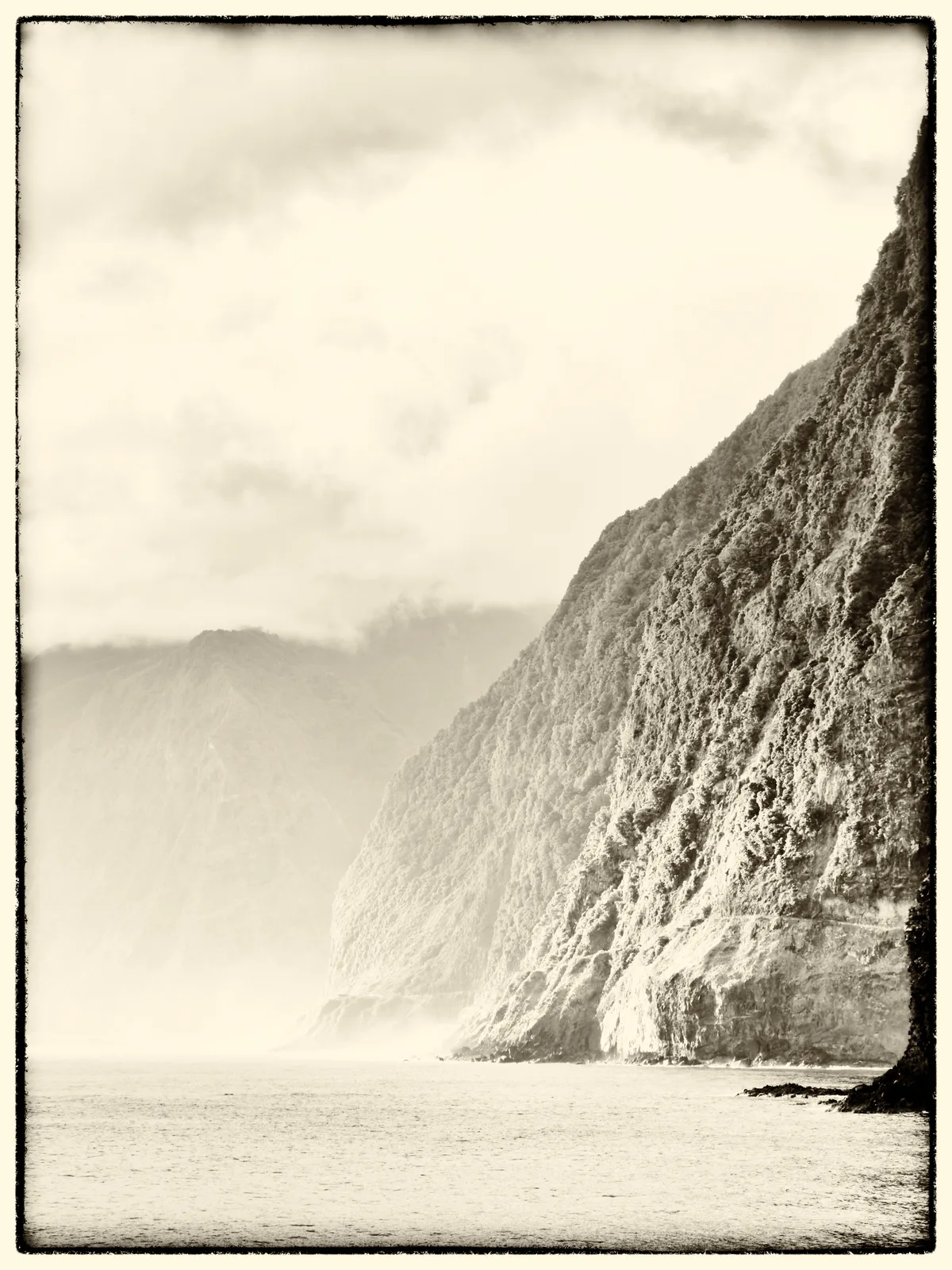 A warm yellowed coastal postcard print with luminous mist, restrained grain, and a worn edge.