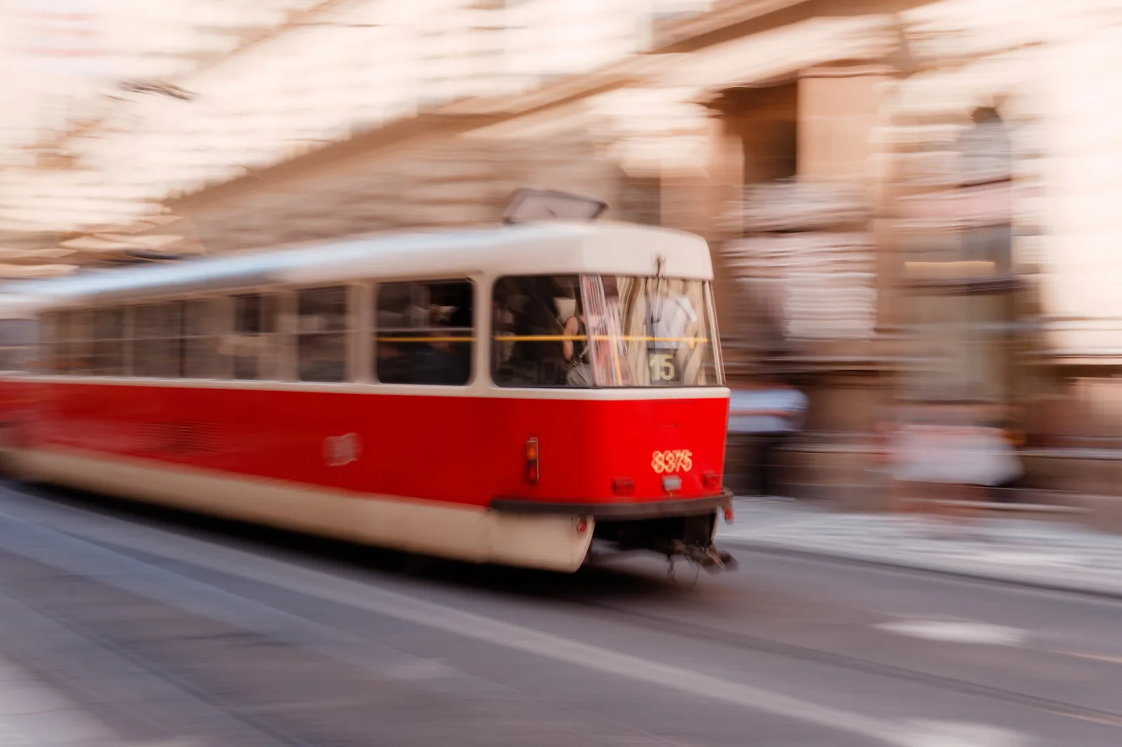 A red Lisboa tram moving through a softly blurred city street.