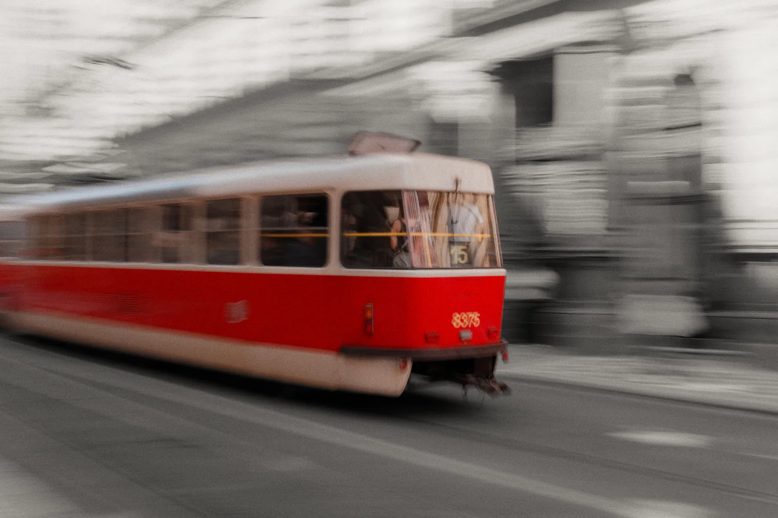 A Lisboa tram in vivid red against a softly sepia monochrome city street.