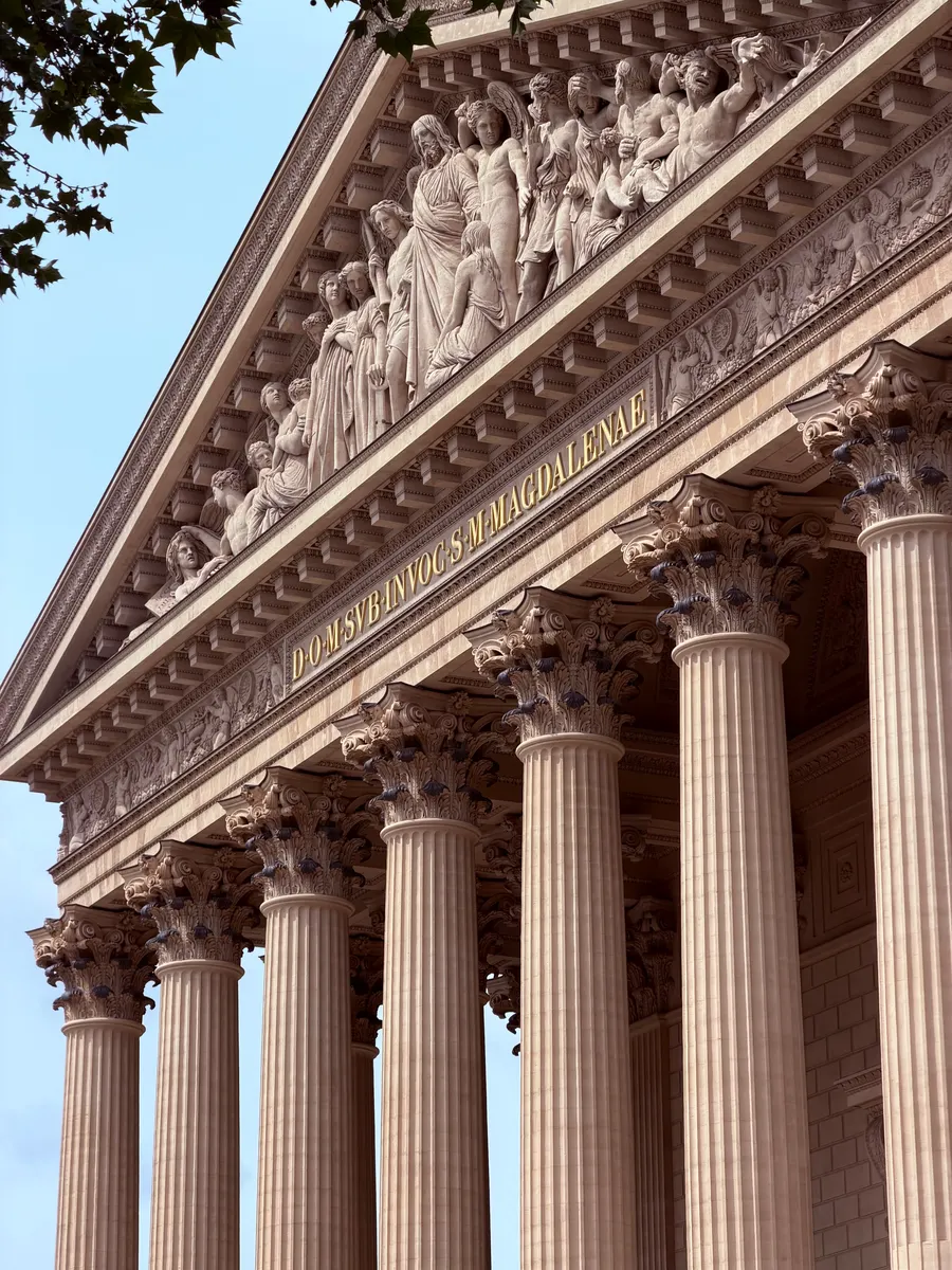 A color photograph looking upward along classical stone columns, a carved pediment, and a Latin inscription.